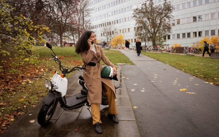 En tjej sitter på en vespa och pratar i telefon.